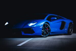 Niebieskie Lamborghini stojące częsciowo w cieniu z odpalonymi lampami
